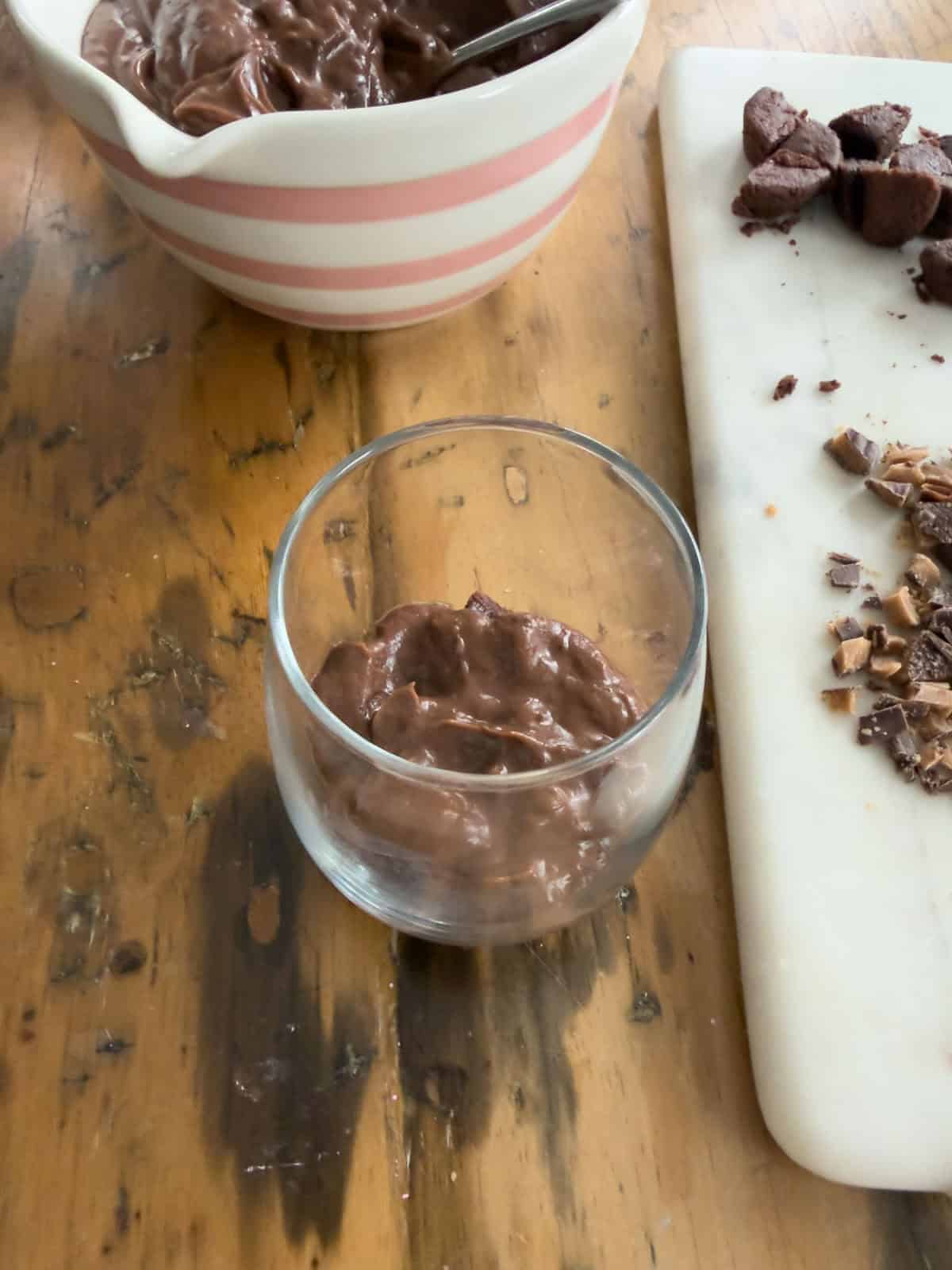 Chocolate pudding layer added over brownie pieces in a clear glass for mini chocolate brownie trifles.