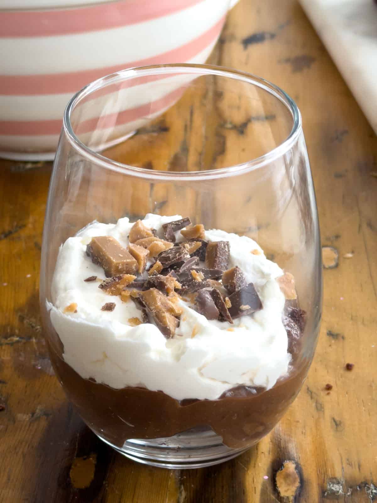 Chopped Skor bar pieces sprinkled over the whipped cream layer in a clear glass mini chocolate brownie trifle.