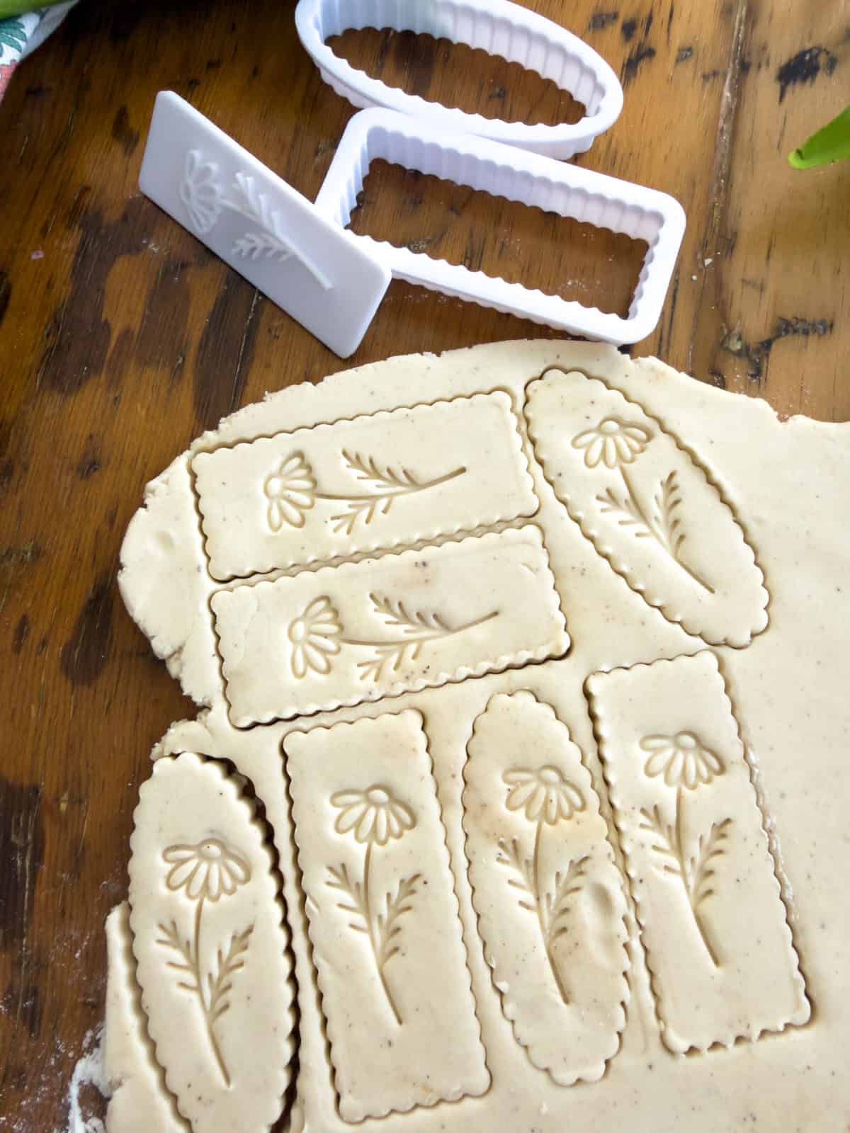 Vanilla shortbread cookie dough rolled out on a floured surface with cookie cutters and cut cookies on a wood table.