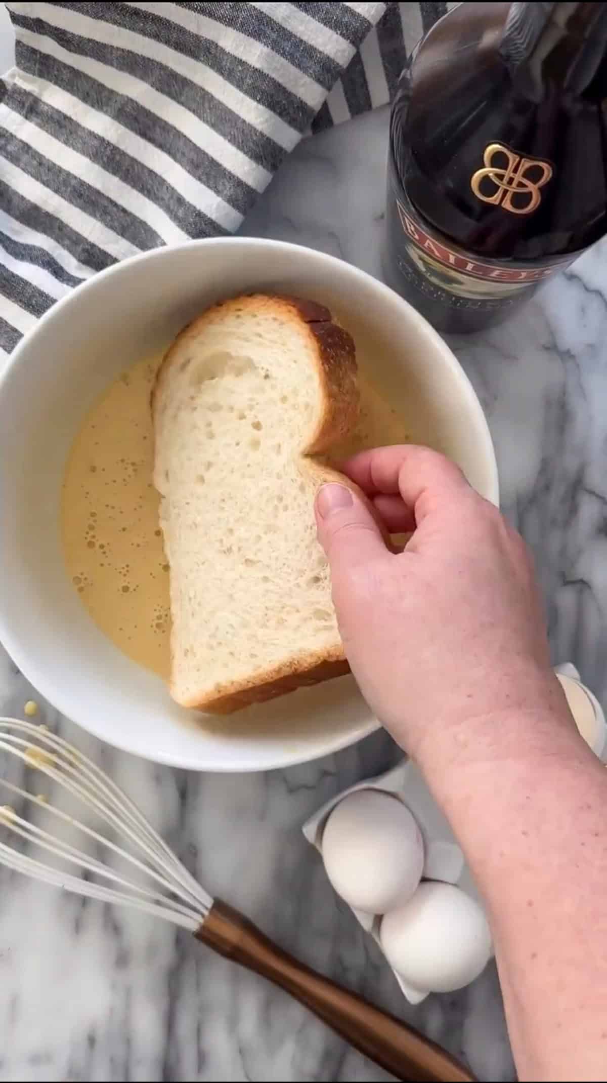Making Baileys French toast by dipping bread into egg mixture.