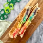 A rainbow grilled cheese sandwich cut in half on a cutting board.