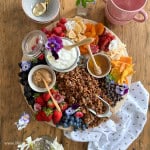 Yogurt parfait board with fresh berries, granola, honey, peanut butter, dried fruit, and edible flowers on a wooden lazy Susan board.