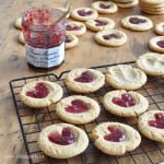 Peanut butter and jam thumbprint cookies on a cooling rack with a jar of jam.