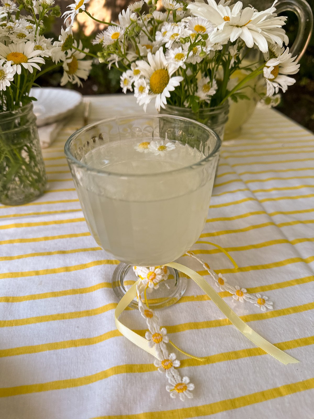 A table with a glass of lemonade decorated with yellow and daisy ribbon.