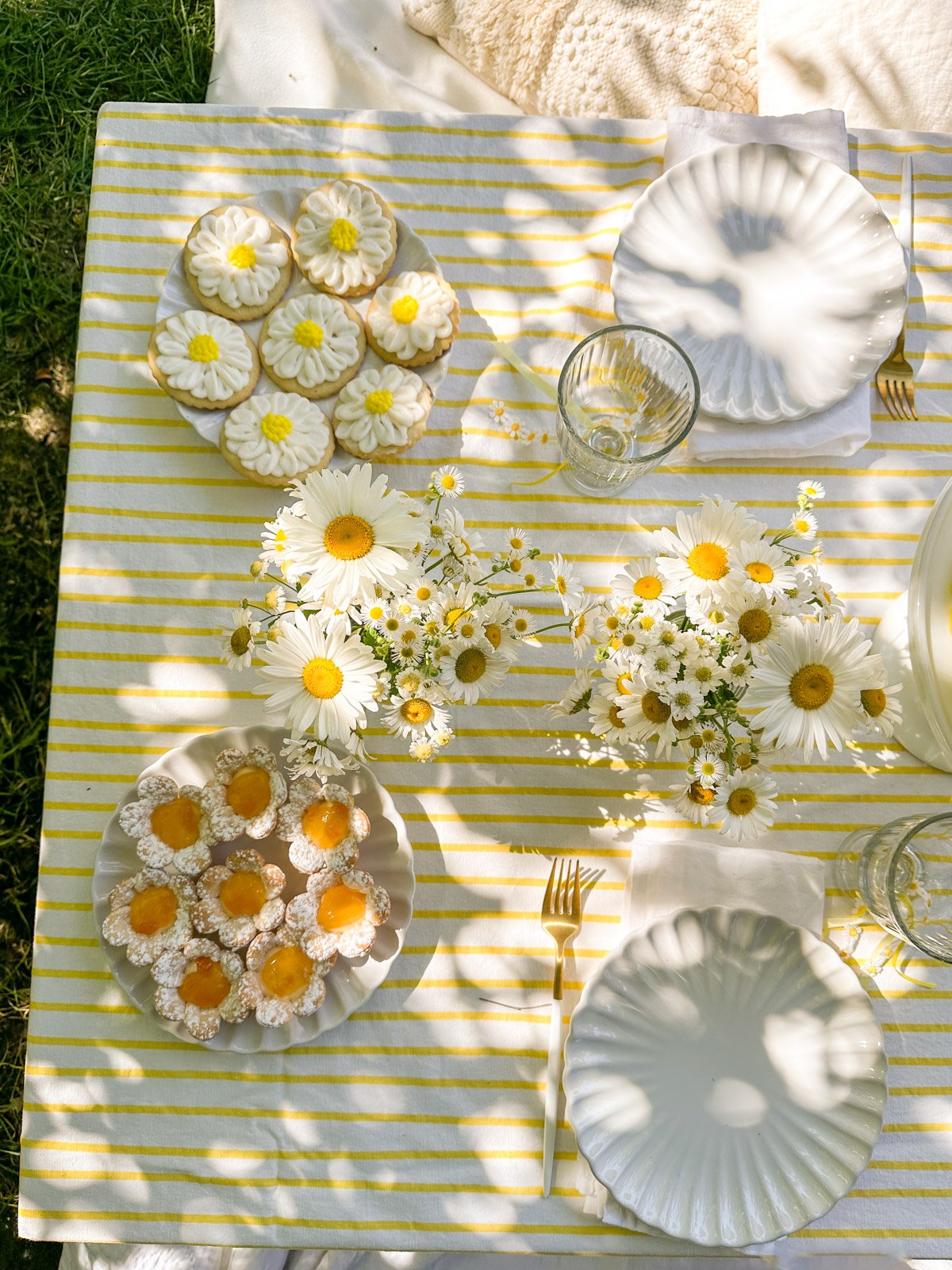 Daisy themd party table with daisy desserts, including cookies and tarts.