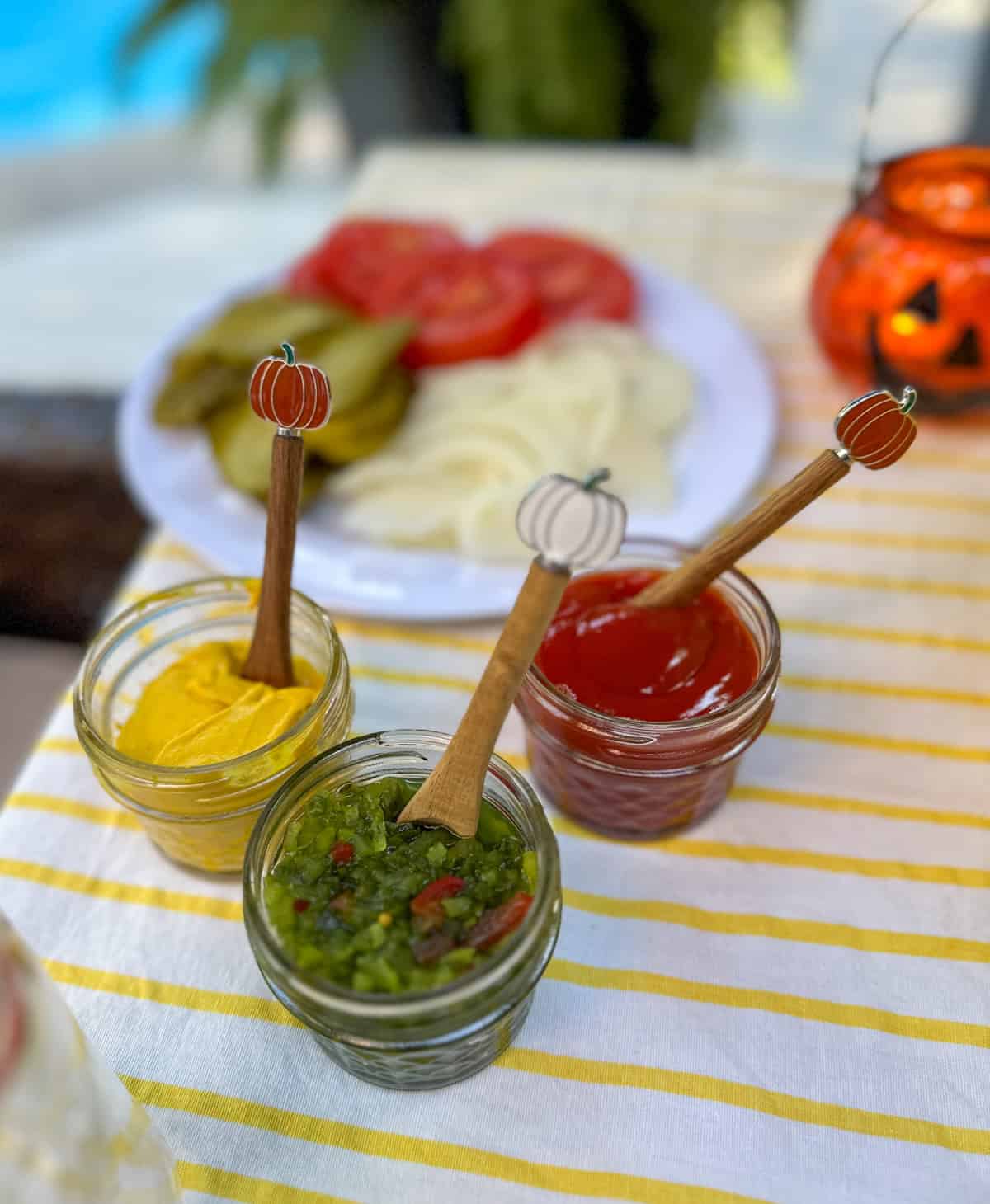 Burger condiments in mini mason jars with pumpkin spoons for a summerween bbq.
