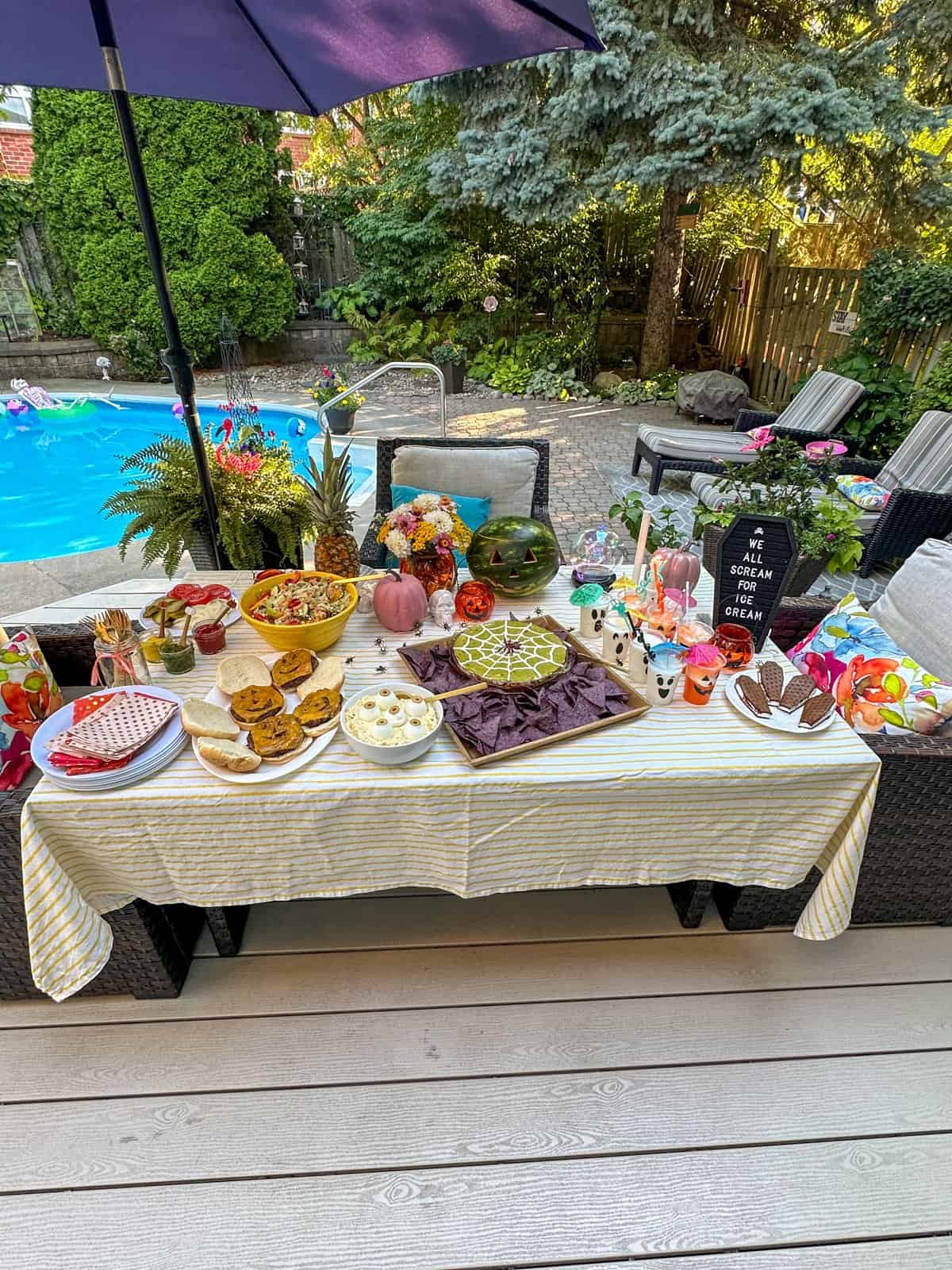 Summerween Halloween BBQ food table with burgers, salads, and drinks.