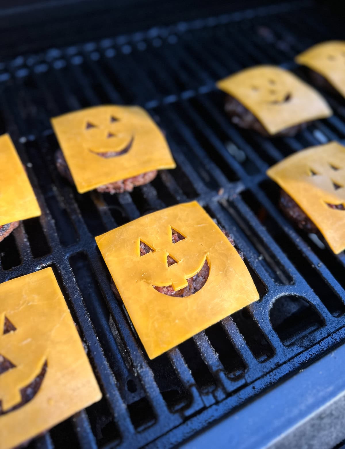 Summerween burgers with jack-o-lantern faces made of cheese.