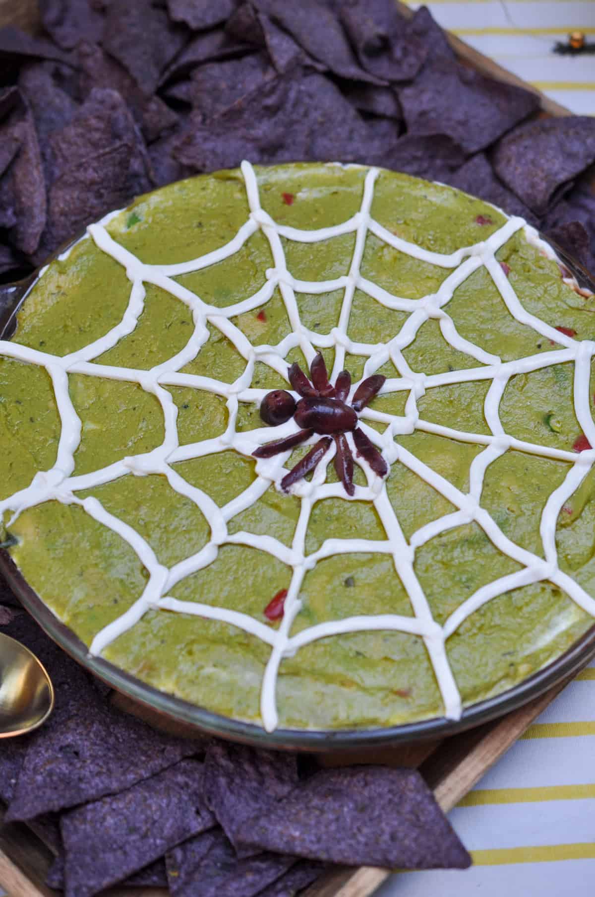 Halloween 7 layer dip with a sour cream spider's web and black olive spider on top.