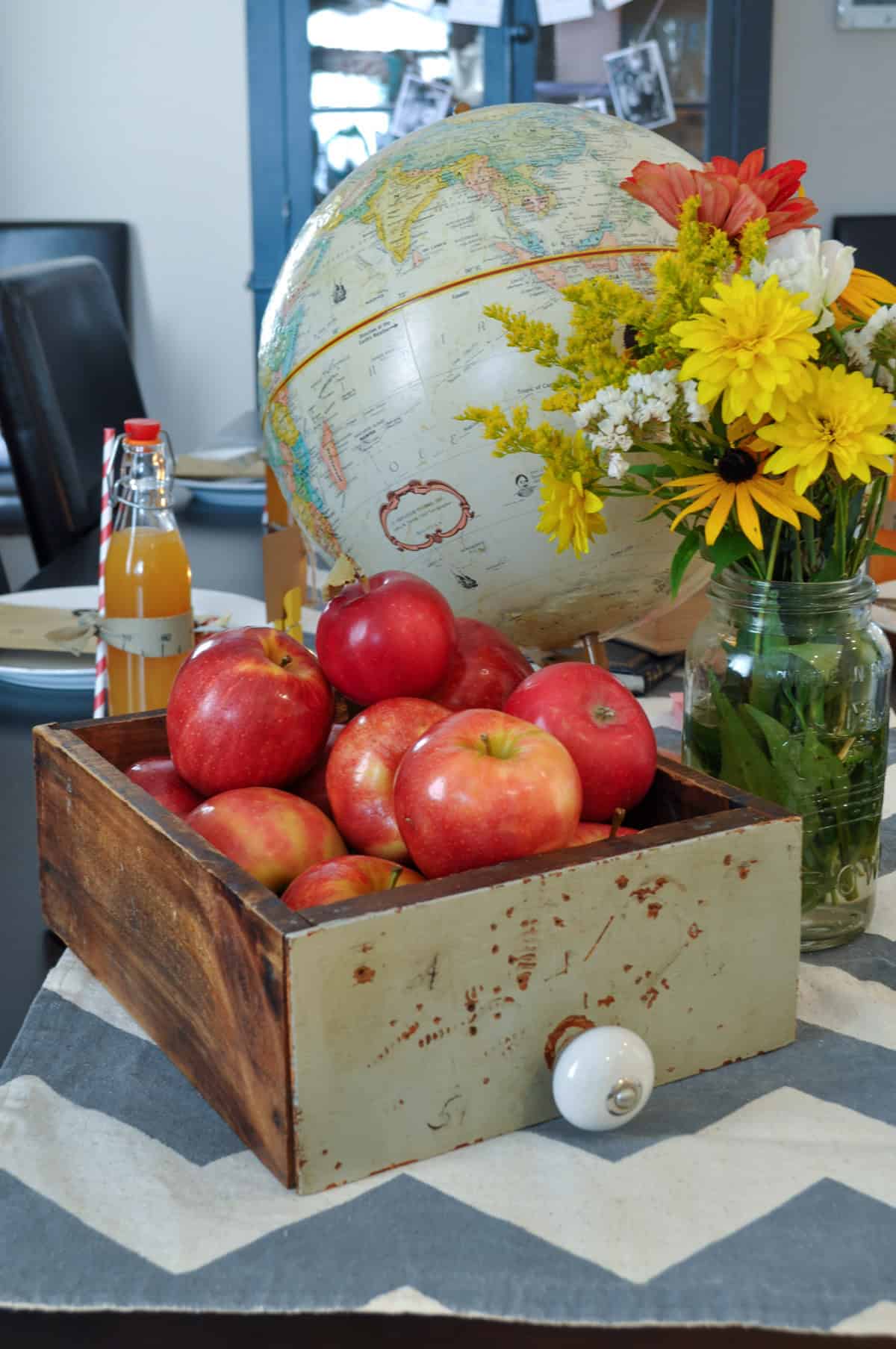 Back to school party center piece with vintage drawer filled with apples, vintage globe, and flowers.