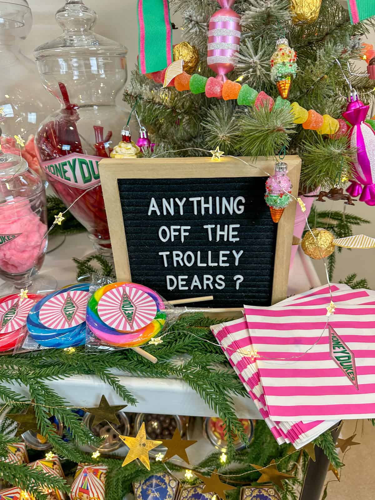 "Anything off the trolley's dears?" sign on a letterboard with a mini candy Christmas tree, and lollipops and candy on a Honeydukes candy cart for Christmas.
