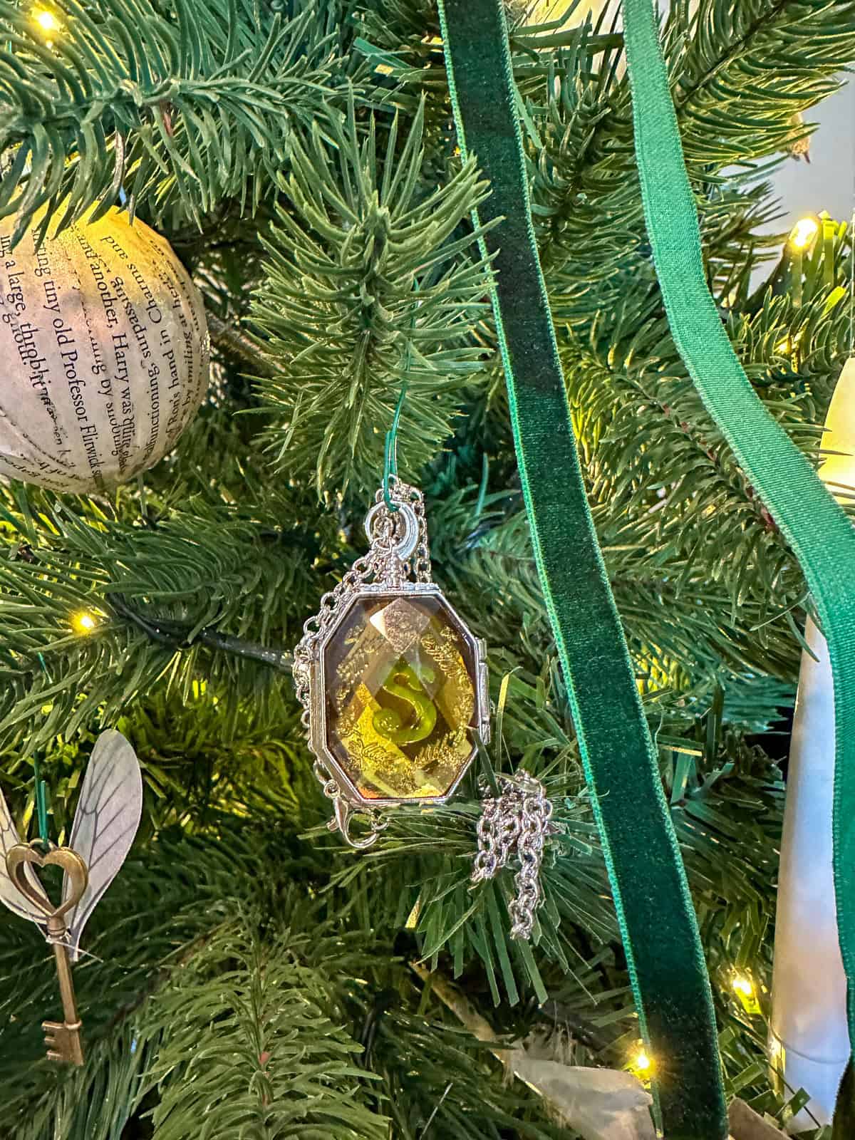 Slytherin locket Horcrux ornament with silver chain and green ribbon on Harry Potter inspired Christmas tree.