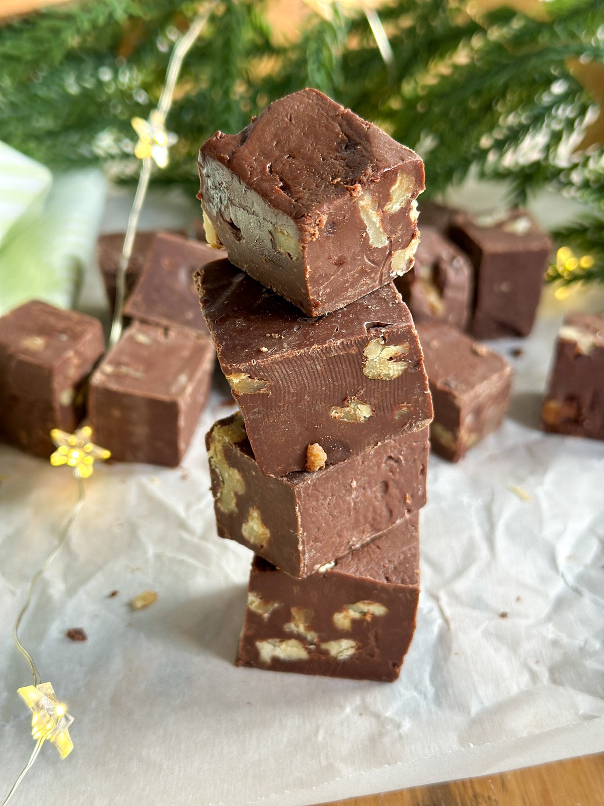 Stack of easy chocolate walnut fudge squares, with more pieces in the background.