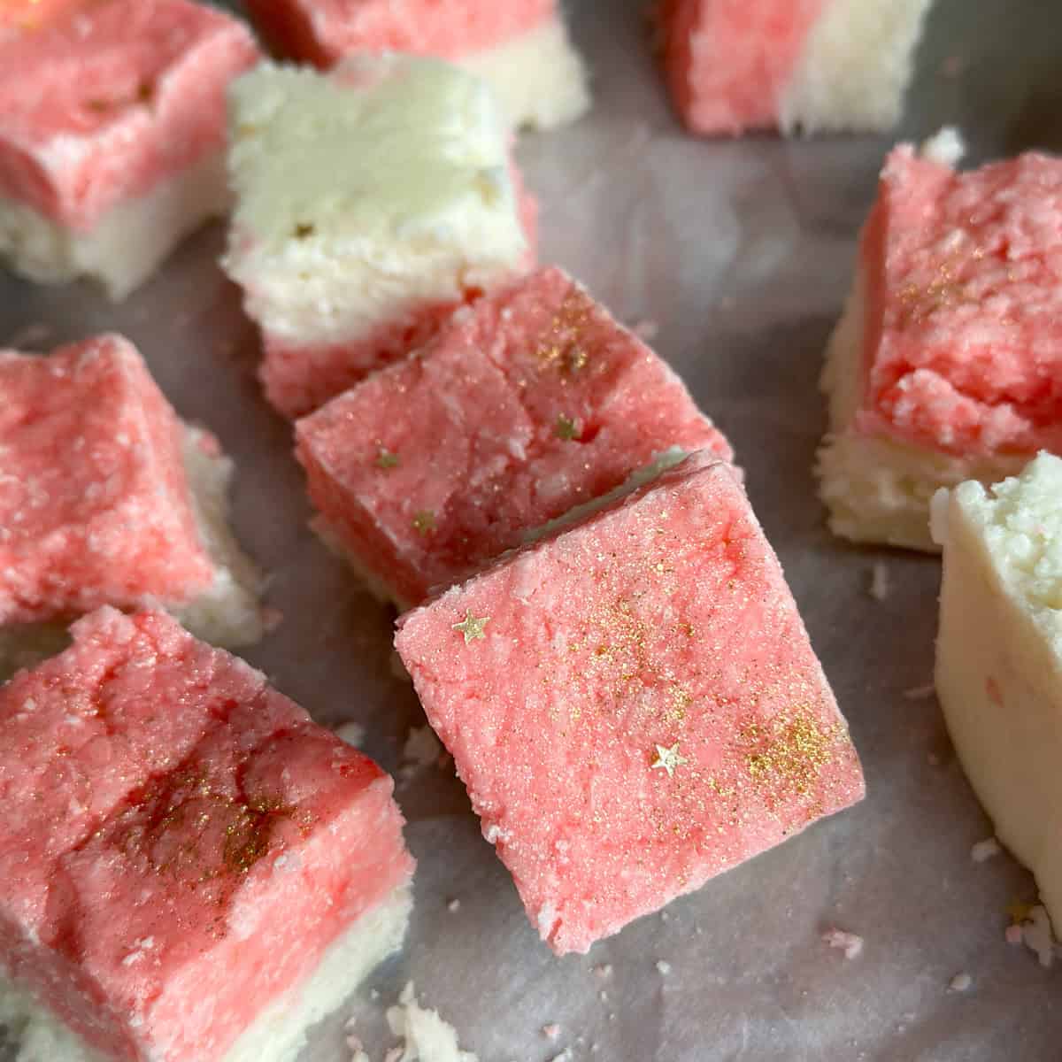 Homemade pink and white coconut ice recipe, cut into squares on a parchment paper.