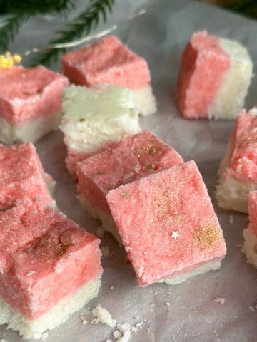 Homemade pink and white coconut ice recipe, cut into squares on parchment paper.