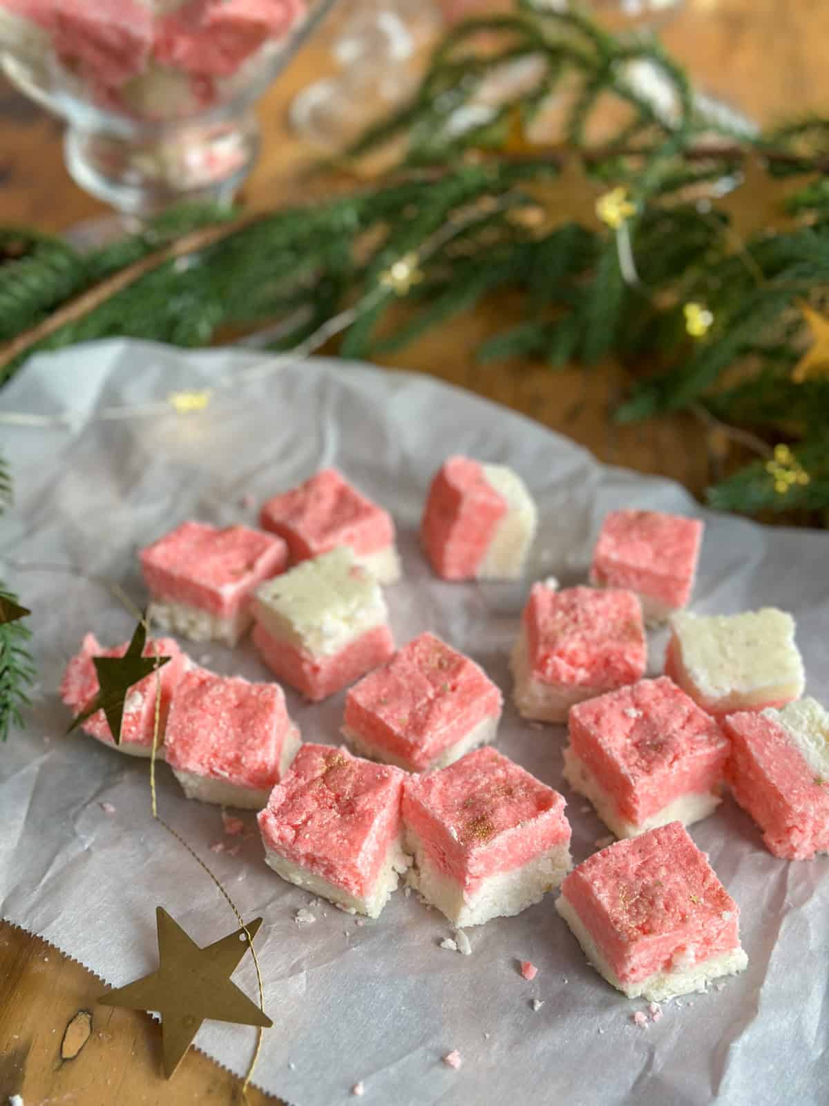 Coconut ice cut into squares on a piece of parchment paper with a glass canister in the background.
