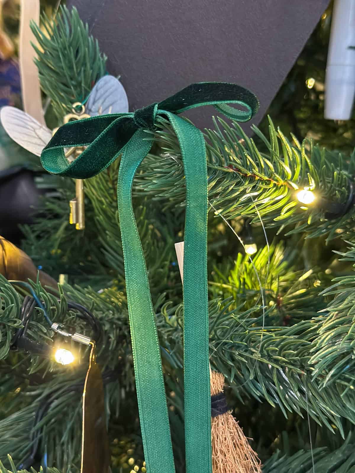 Slytherin green velvet ribbon bow tied on Harry Potter Christmas tree with flying key ornament and twinkling lights.