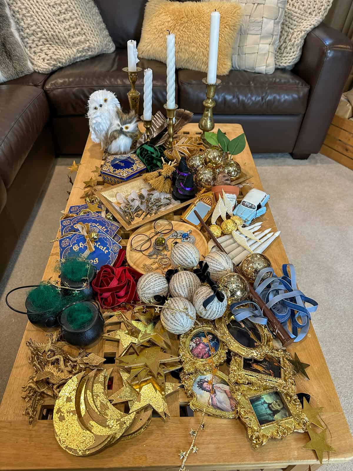 Collection of DIY Harry Potter Christmas ornaments on coffee table including book page balls, chocolate frogs, portrait frames, gold stars, house ribbons, and owl decorations.
