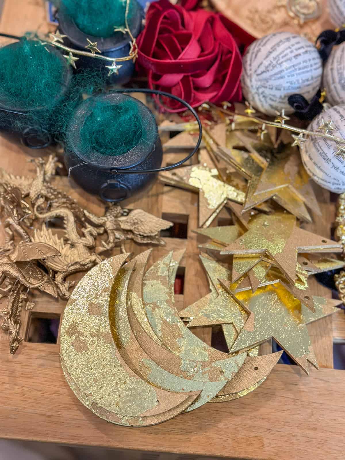 DIY gold stars and moons ornaments with glitter finish alongside cauldrons, velvet ribbons, and book page balls for Harry Potter themed Christmas tree.