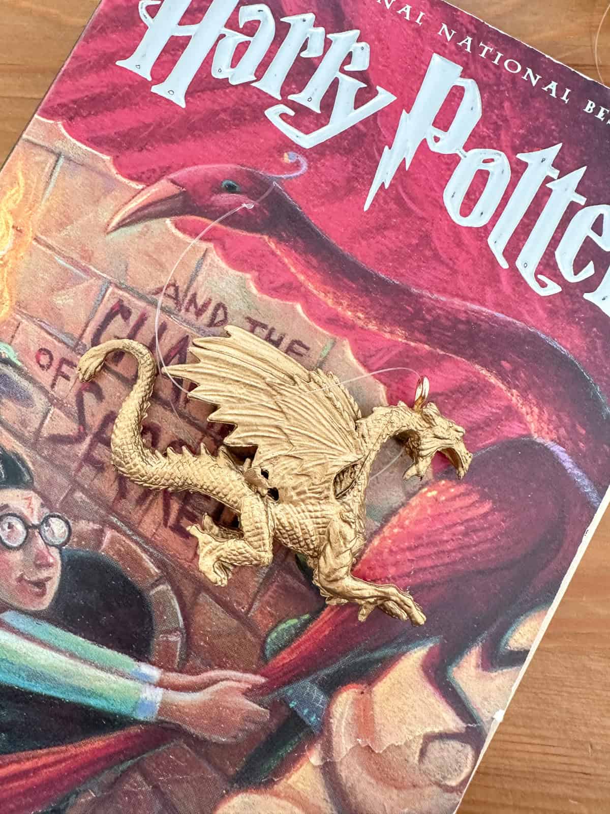 Gold spray painted dragon ornament on Harry Potter and the Sorcerer's Stone book for homemade Harry Potter ornaments and themed Christmas decorations.