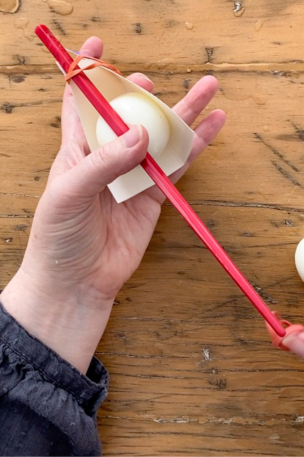 Chopstick and rubber bands shaping warm hard boiled egg into heart shape in milk carton.