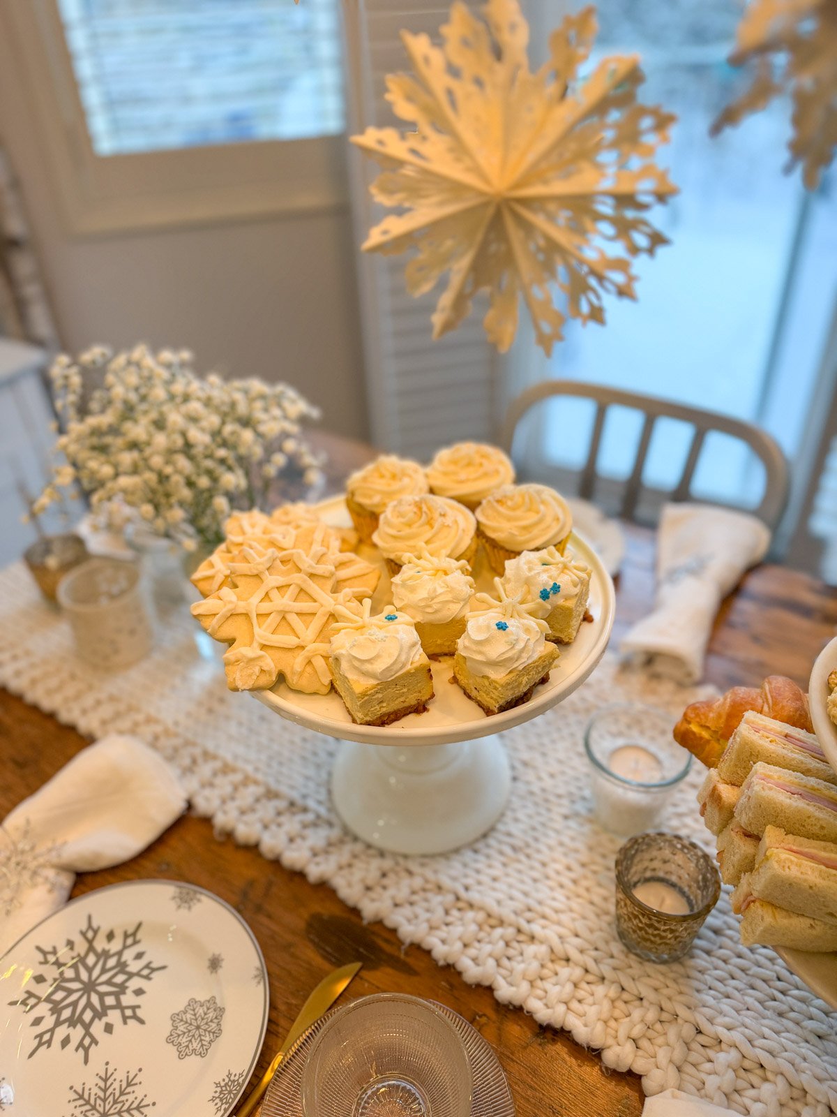 Plate of snow themed desserts at a winter tea party, including snowflake cookies, cheesecake, and cupcakes.