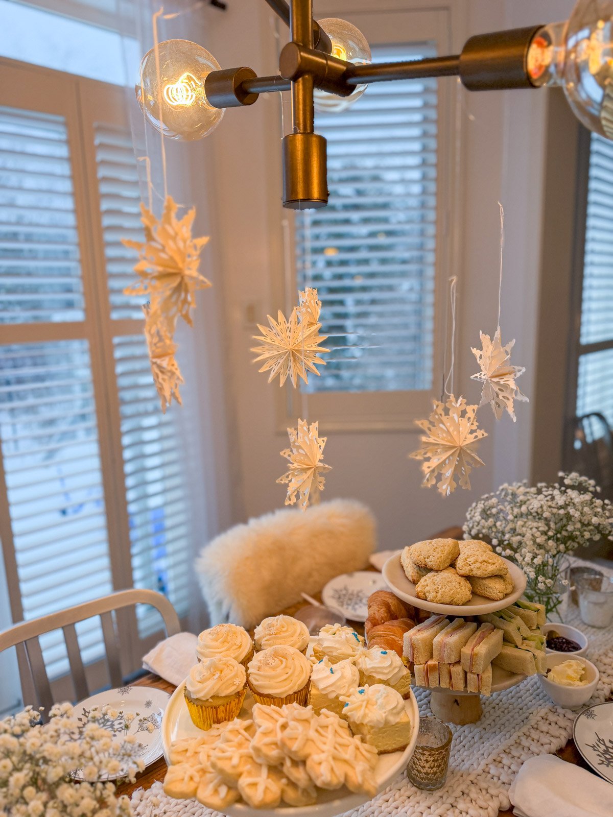 Paper snowflakes hanging from a chandelier over a snow-themed table for a winter tea party.