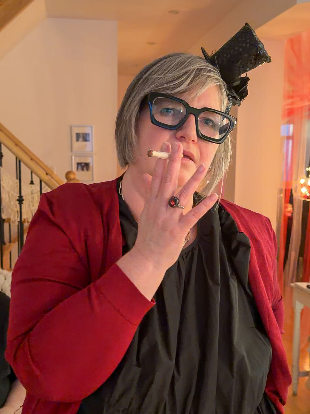 Circus party host in circus chic attire with a mini top hat posing with a chocolate cigarette pretzel rod, with the red and pink tulle big top tent visible in the background.