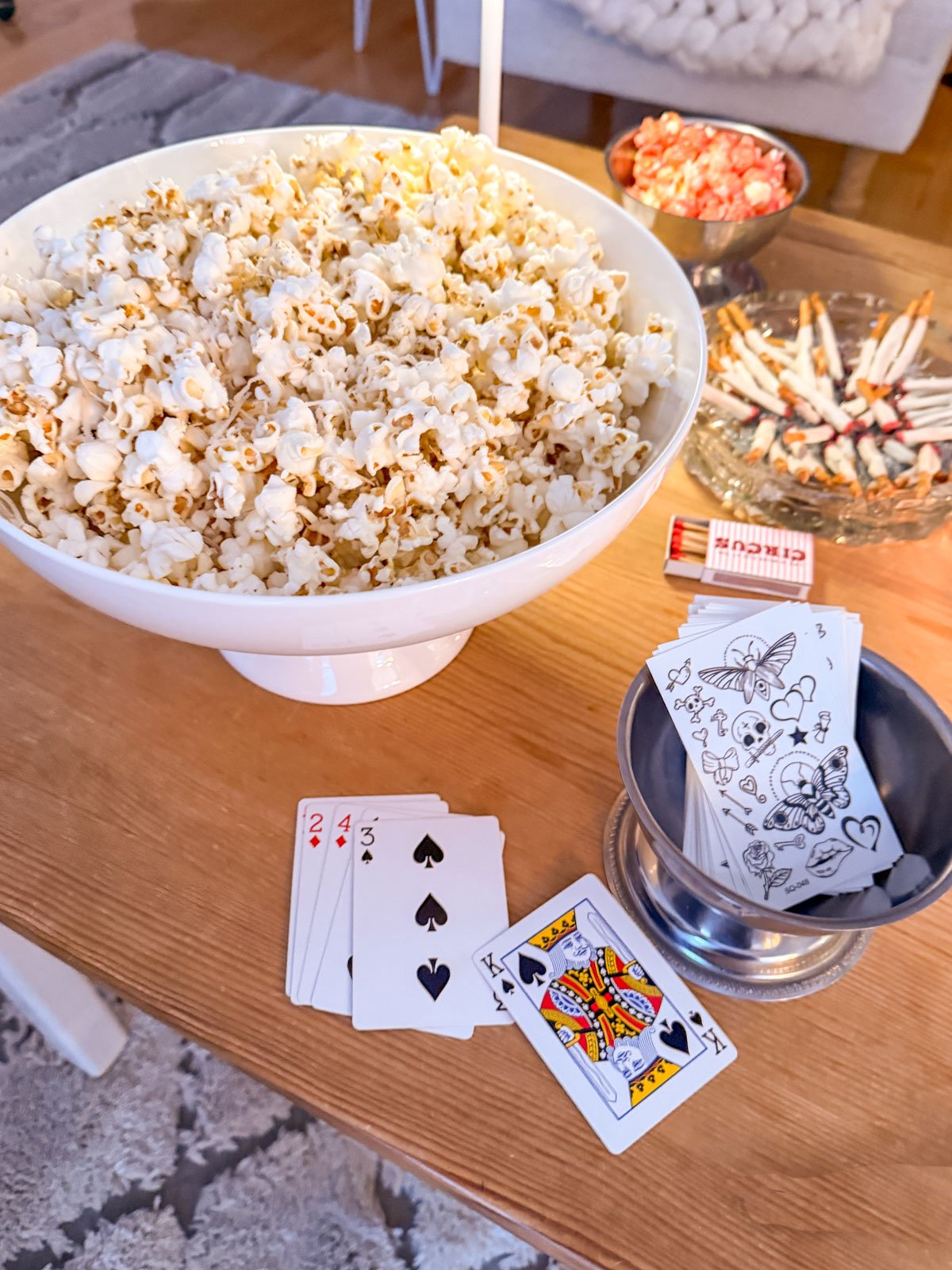 Truffle butter popcorn served in a large white bowl as part of a circus themed cocktail hour spread with playing cards and party decor.
