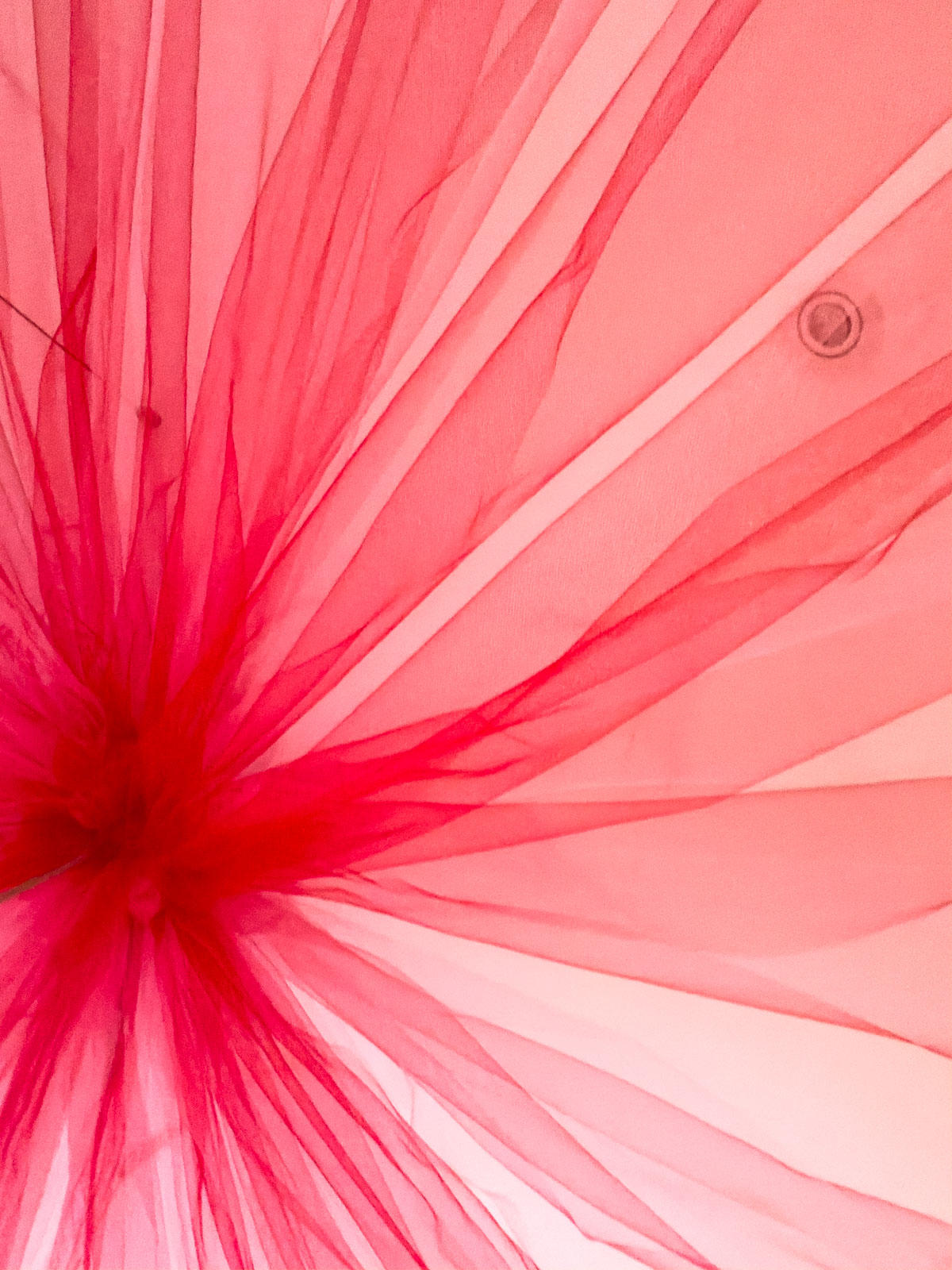Circus party DIY tulle tent ceiling center showing pink and red fabric gathered at light fixture radiating outward.