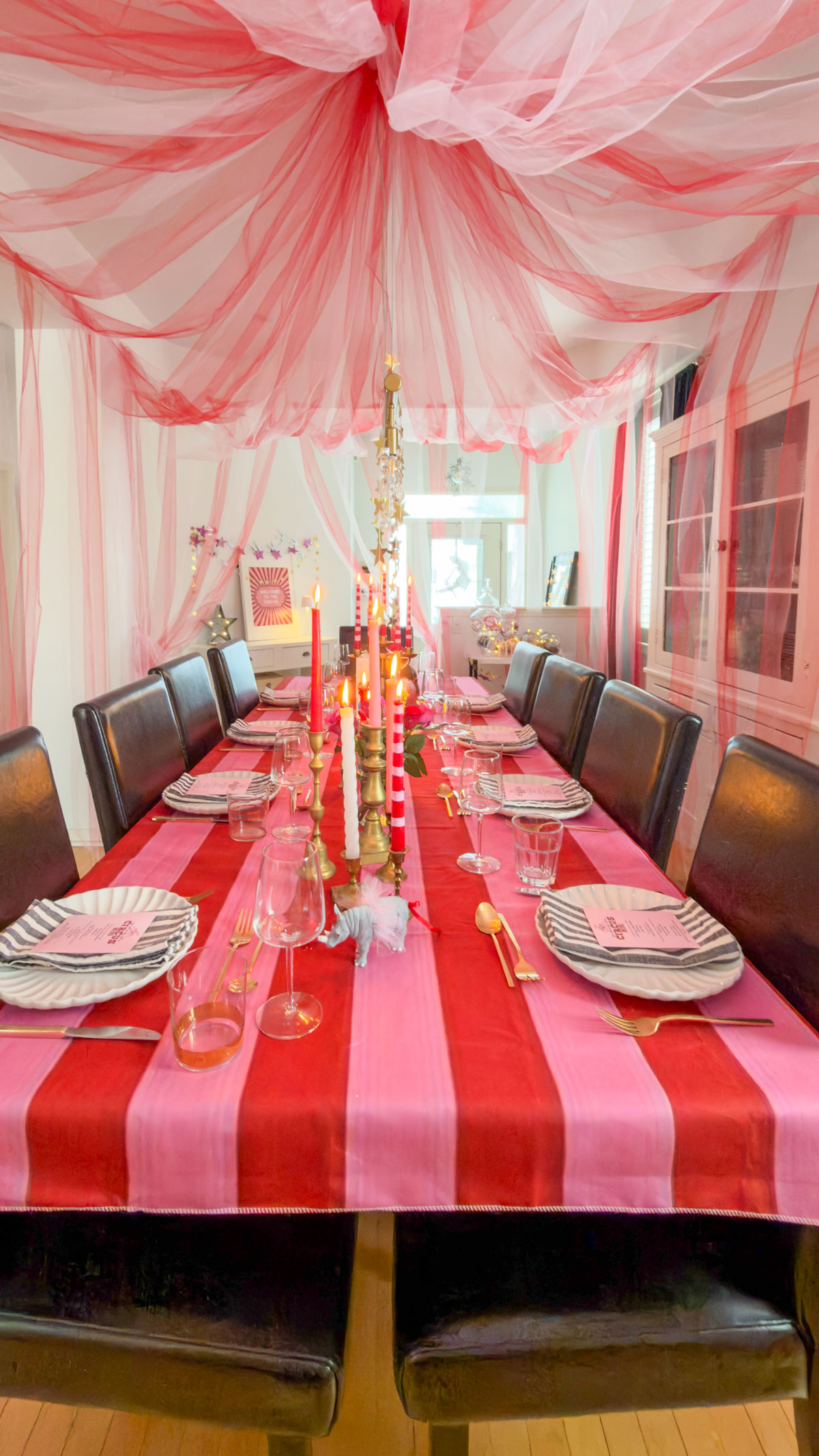 Circus themed dinner party room setup showing pink and red tulle tent ceiling over decorated table.