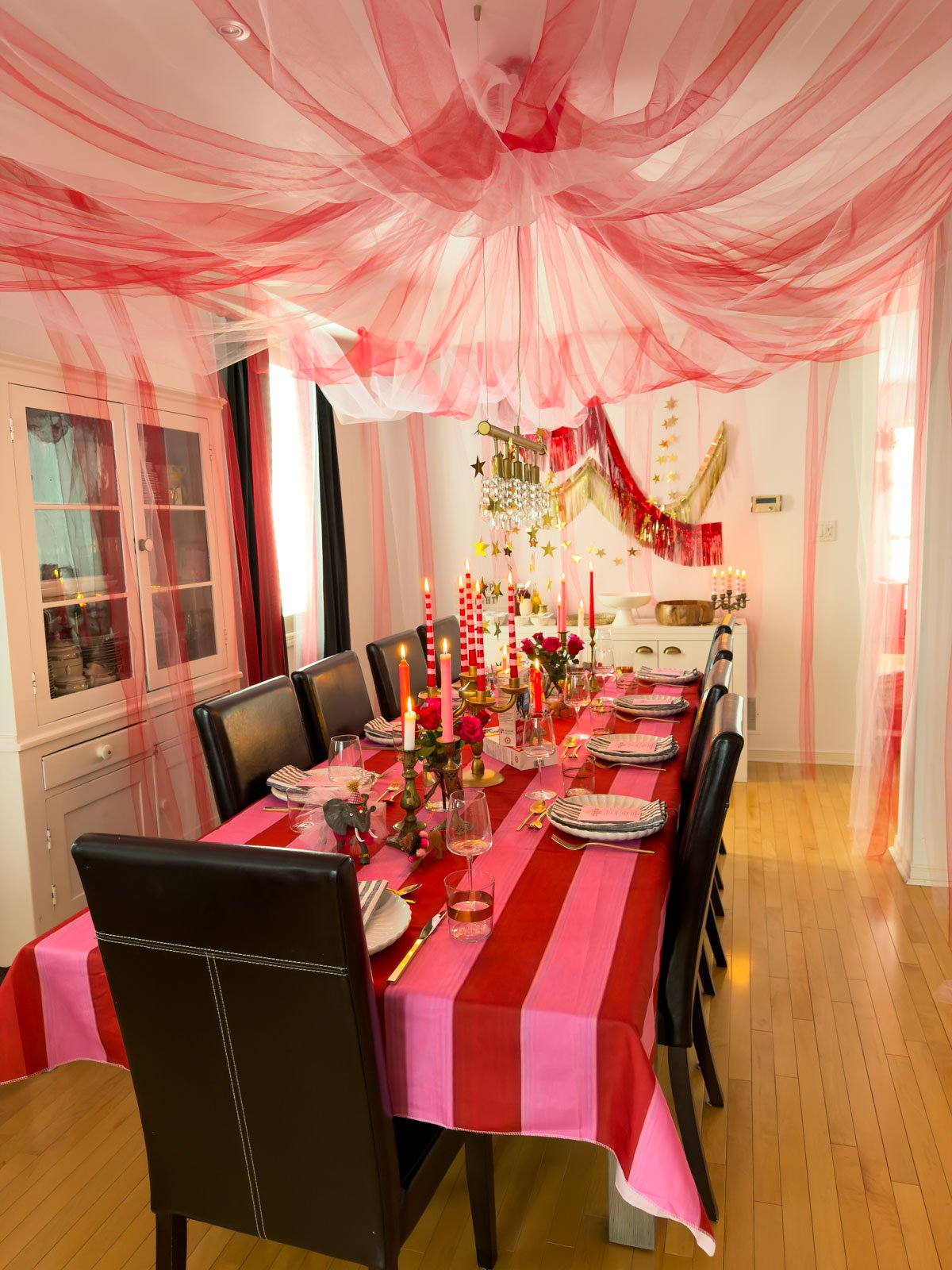 Circus themed dinner party with complete tulle big top tent over dining table featuring striped tablecloth, brass candlesticks and roses.