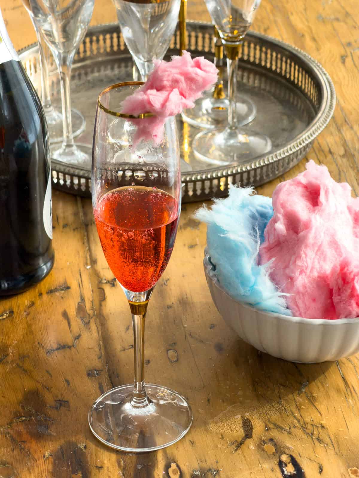 Finished cotton candy cocktail in gold-rimmed champagne flute with pink cotton candy garnish on rim.