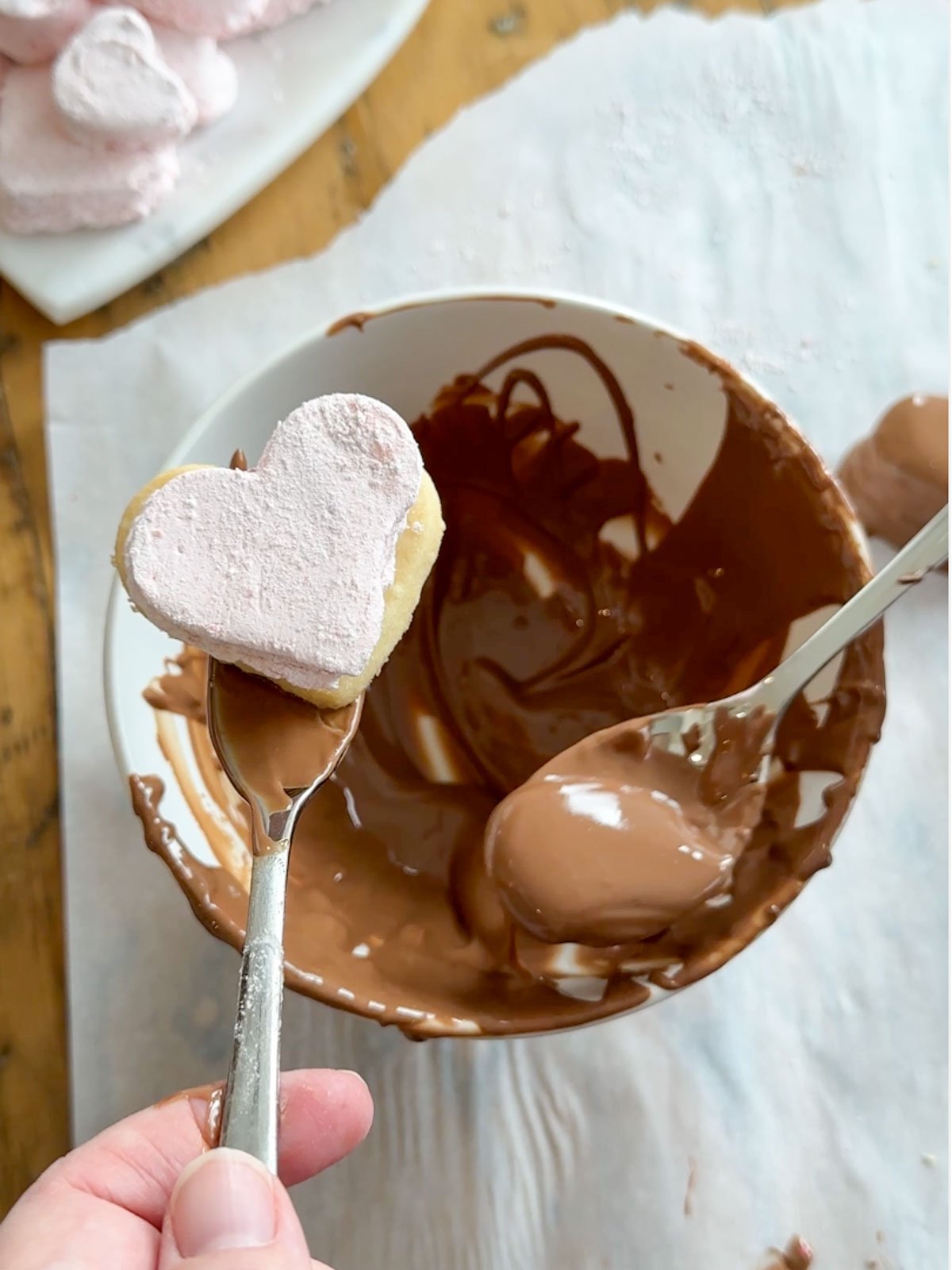 Strawberry marshmallows being dipped in melted chocolate.