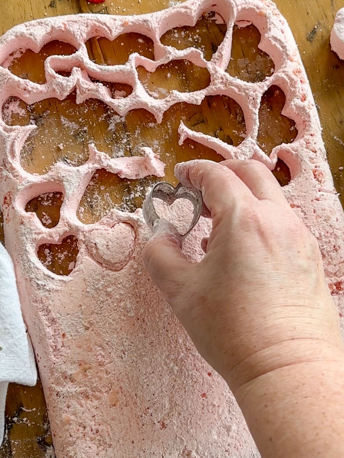 Cutting multiple heart-shaped strawberry marshmallows with cookie cutter for Valentine's Day.