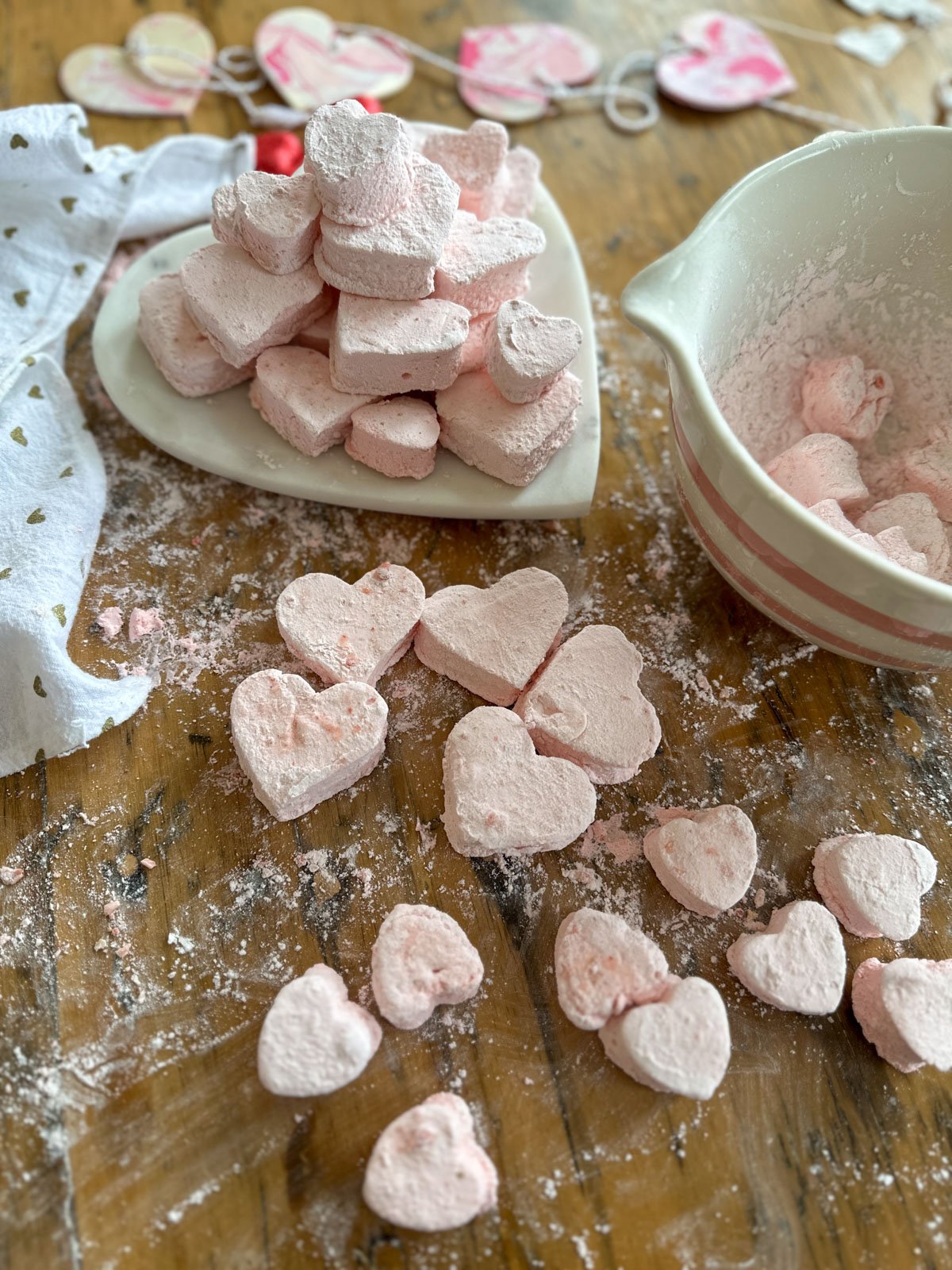 Homemade strawberry marshmallows in heart and flower shapes on white plates for Valentine's Day.
