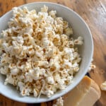 Truffle butter popcorn in a white bowl with a wedge of Parmesan cheese on a rustic wood surface.
