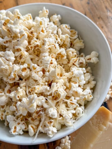Truffle butter popcorn in a white bowl with a wedge of Parmesan cheese on a rustic wood surface.