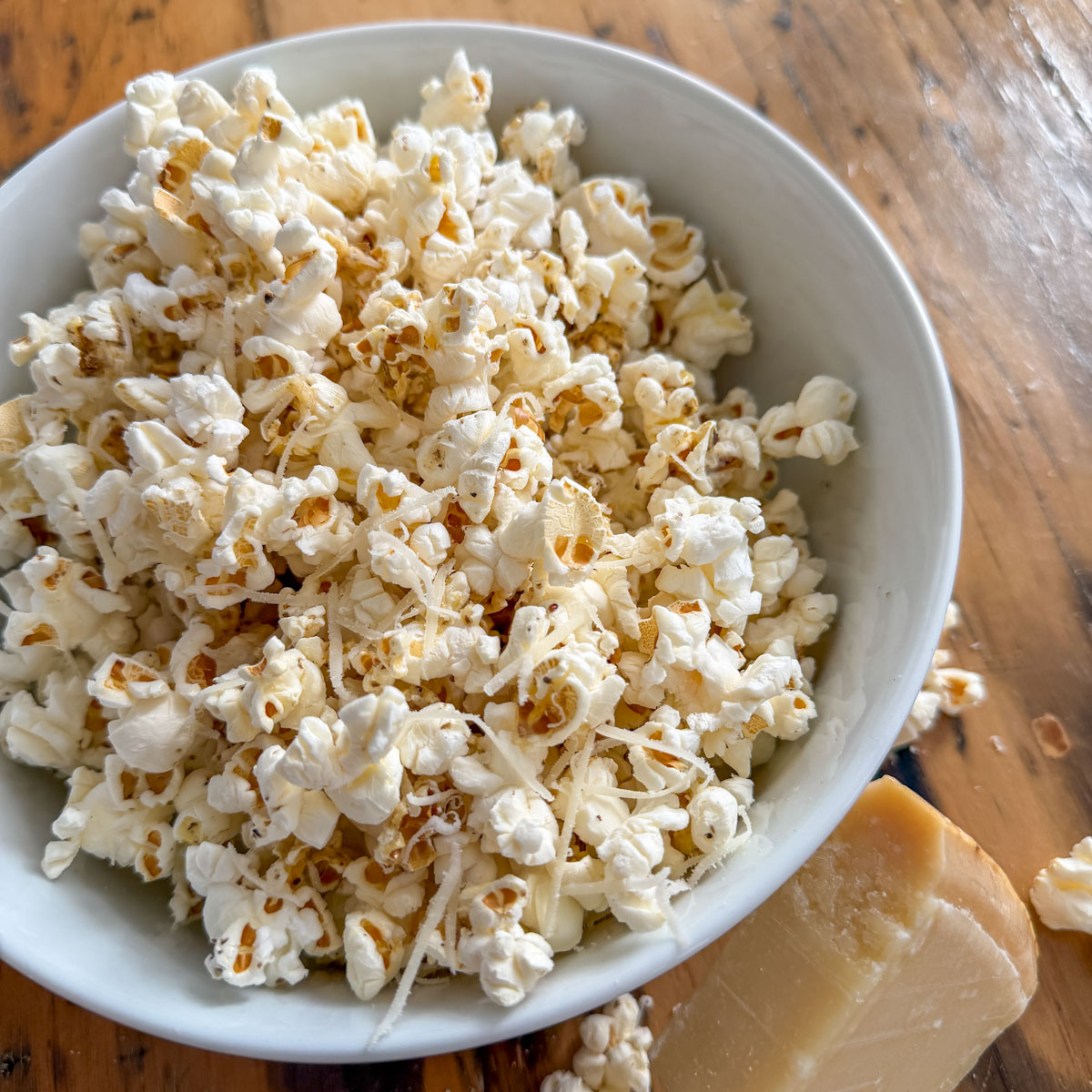 Truffle butter popcorn in a white bowl with a wedge of Parmesan cheese on a rustic wood surface.