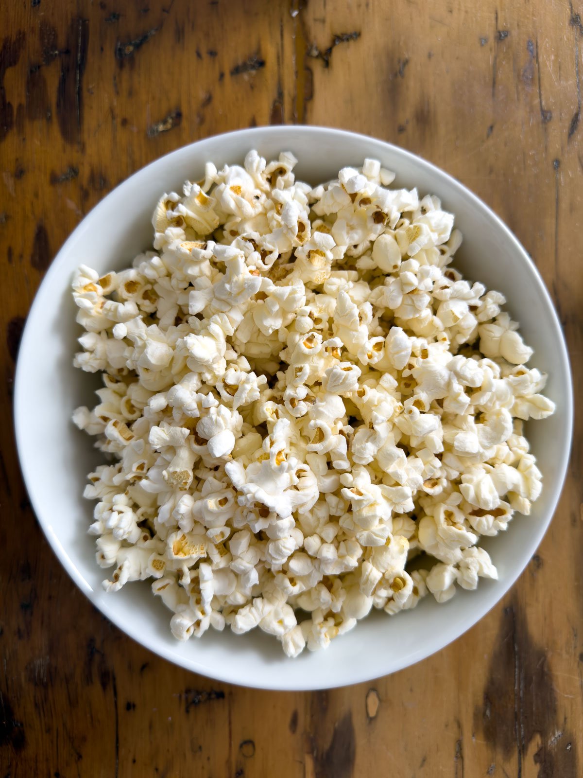 Plain air-popped popcorn in a white bowl on a rustic wood surface, ready for truffle butter seasoning.