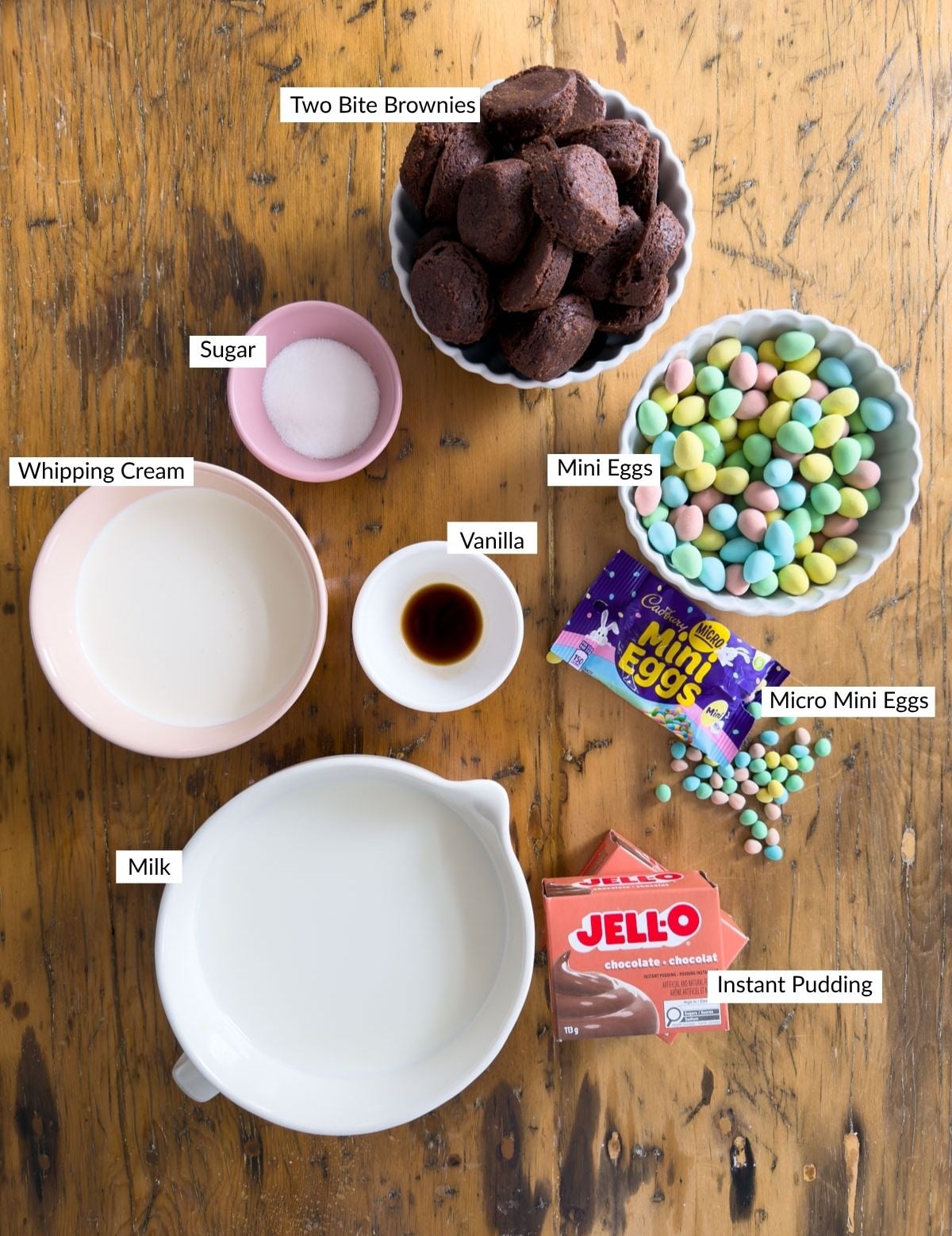 Ingredients for Easter trifle including two-bite brownies, Cadbury mini eggs, Cadbury micro mini eggs, Jell-O chocolate pudding, whipping cream, sugar, and vanilla.