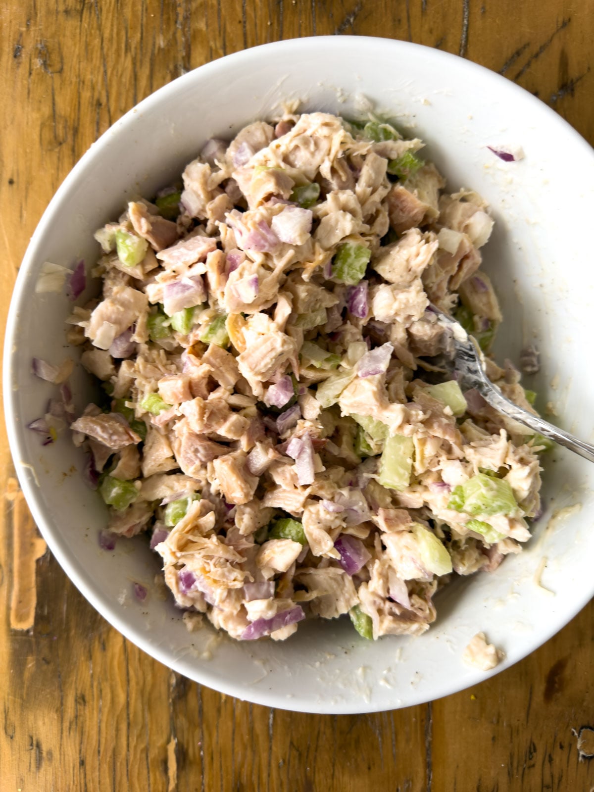 Finished chicken salad filling in a white bowl with a spoon, ready for chicken salad finger sandwiches.