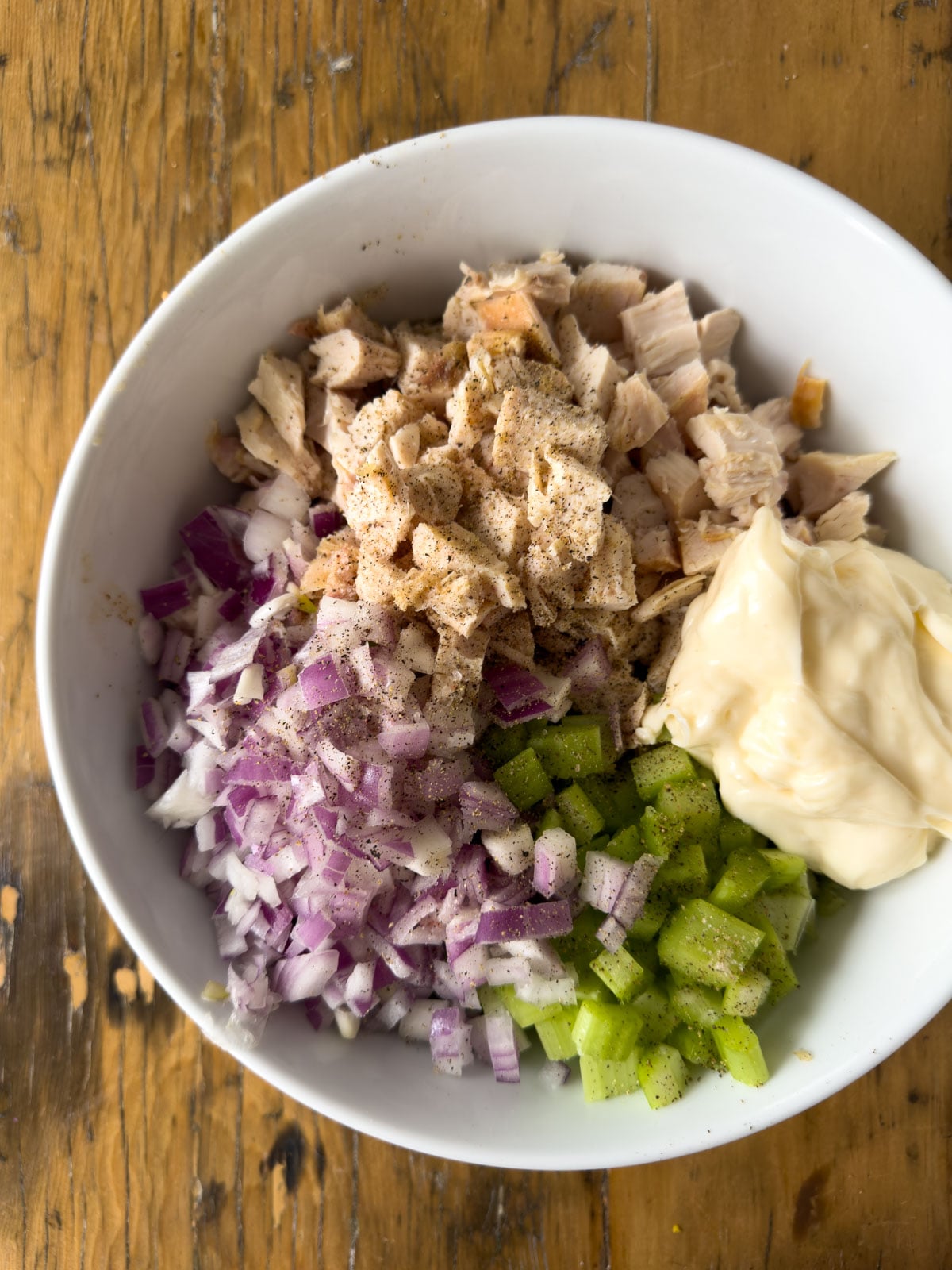 Chicken, diced celery, red onion, and mayonnaise in a white bowl before mixing for chicken salad finger sandwiches.