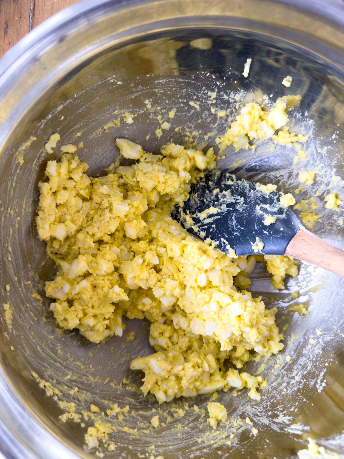 Egg salad mixture combined with homemade salad dressing in a stainless steel bowl with a spatula.
