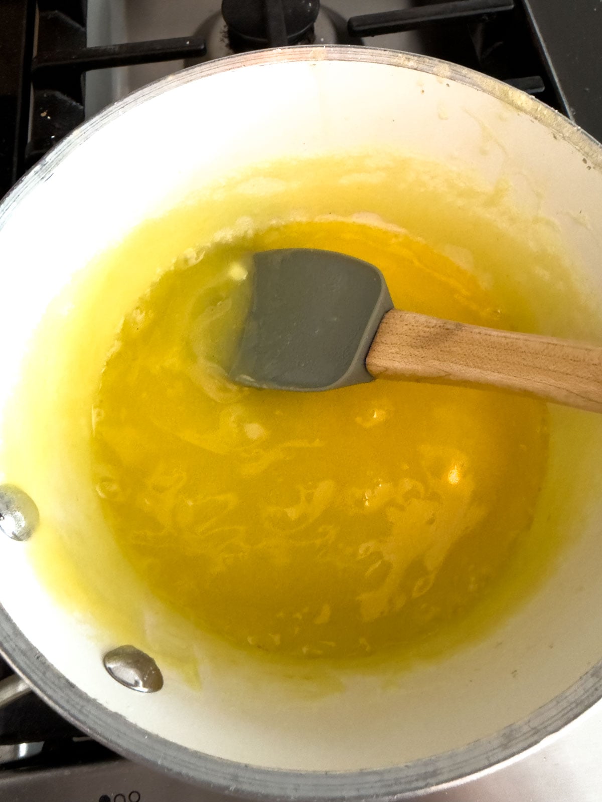 Homemade salad dressing cooking and bubbling in a white saucepan on the stove.