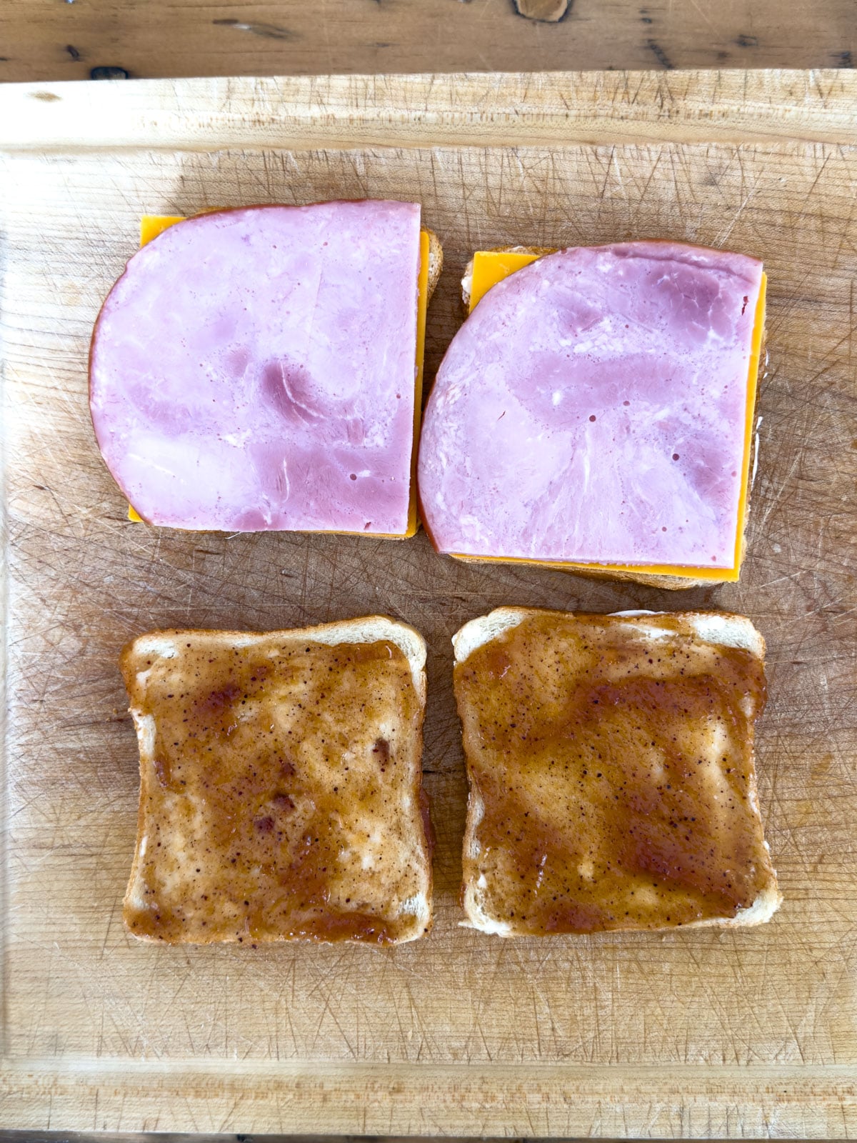 Open-face thick cut ham and cheddar sandwiches with apple butter spread on a wooden cutting board.