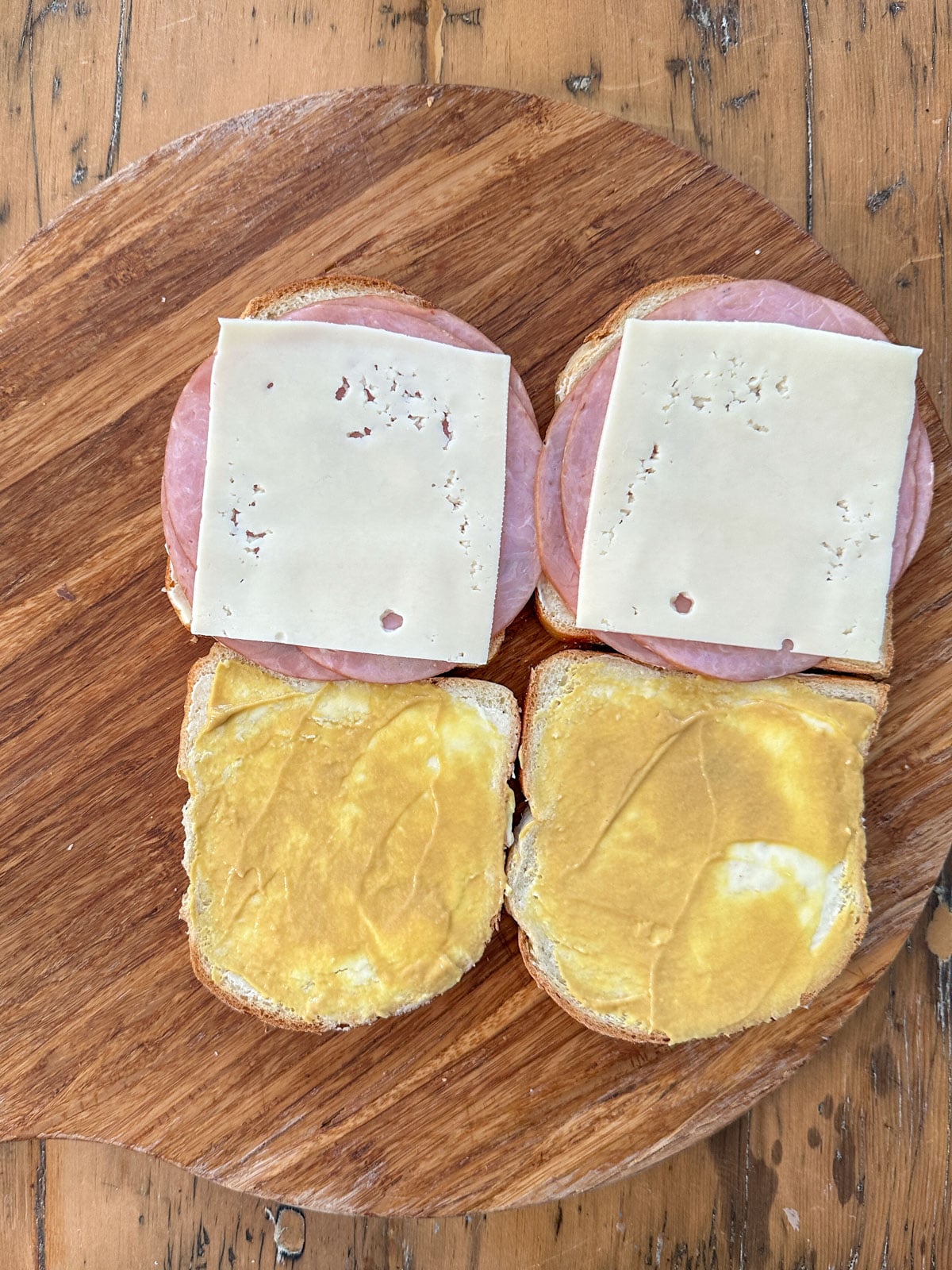 Open-face honey ham and Swiss sandwiches with honey mustard spread on a round wooden board ready to be assembled.