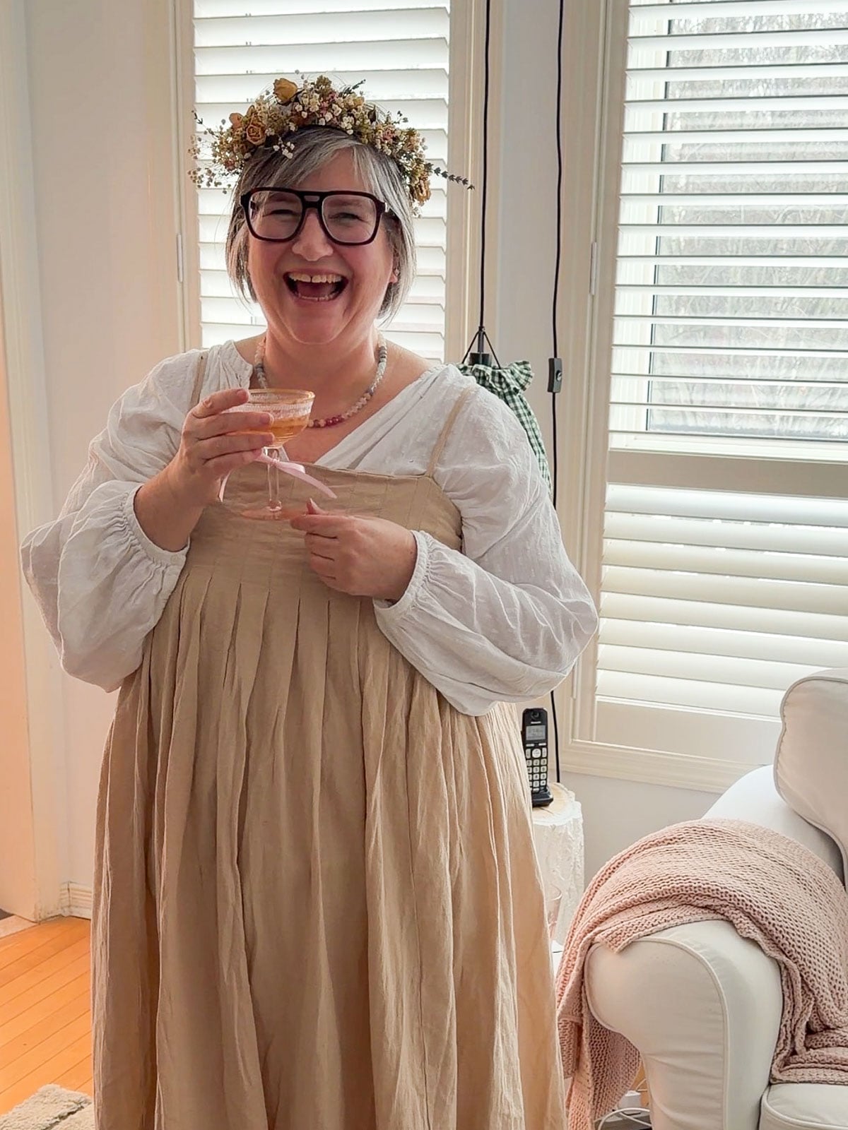 Host laughing at her Little Women vintage tea party wearing a floral dress and dried flower crown.
