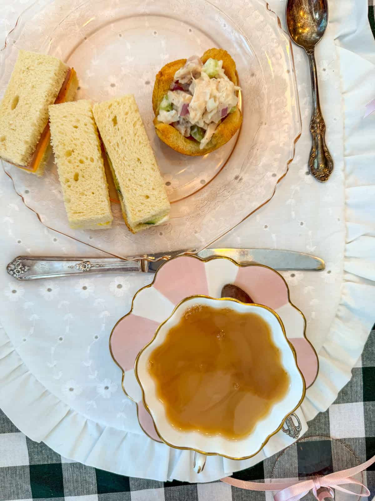 Chicken salad finger sandwiches on a vintage tea party place setting with floral teacup and pink plate.