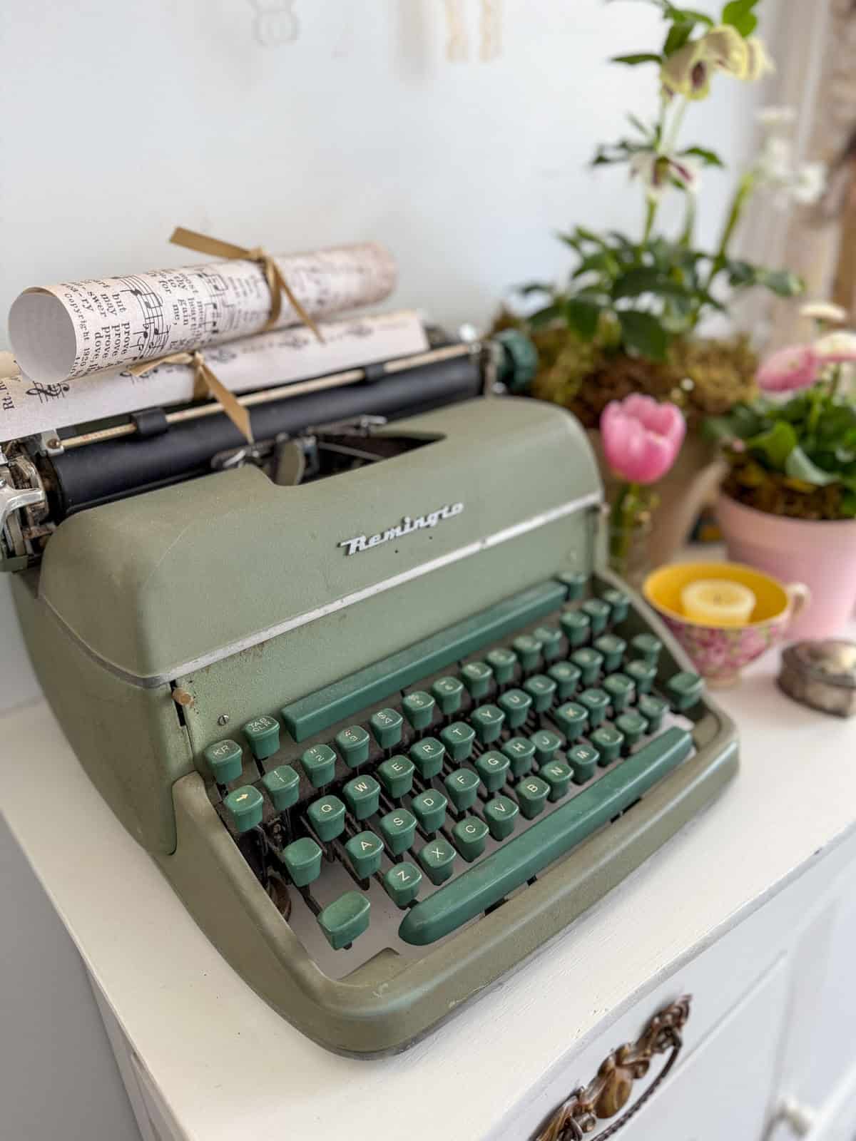 Sage green Remington typewriter with rolled sheet music tied in ribbon representing Jo March at a Little Women vintage tea party.